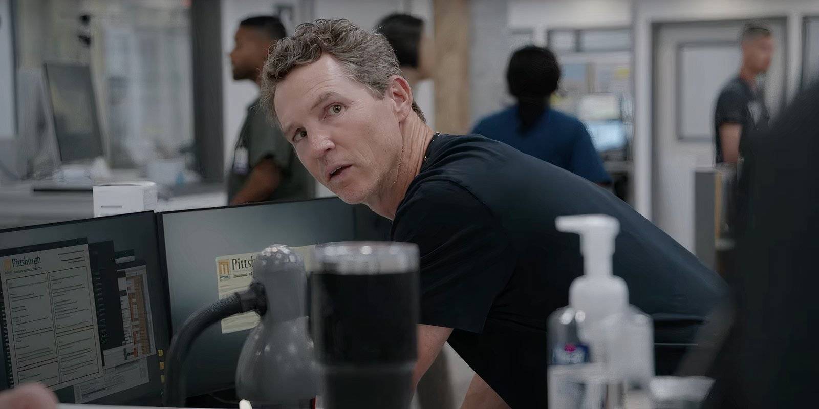 Мужчина-врач наклоняется над компьютером в больнице в *The Pitt*