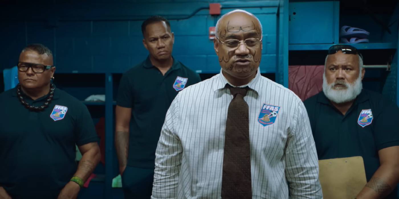 Дэвид Фейн, стоящий сзади и слушающий менеджера в "Next Goal Wins"