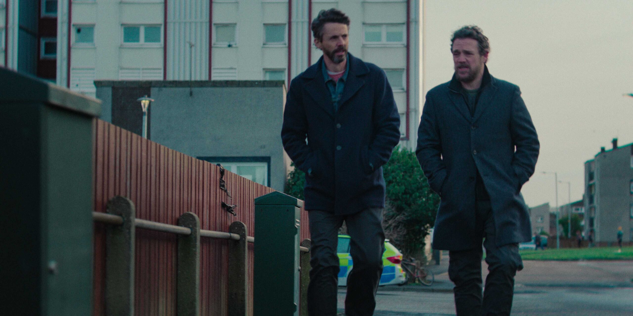 Детектив Карл Морк (Мэттью Гуд) и детектив Харди (Джейми Сайс) идут по улице в 1 сезоне Dept. Q