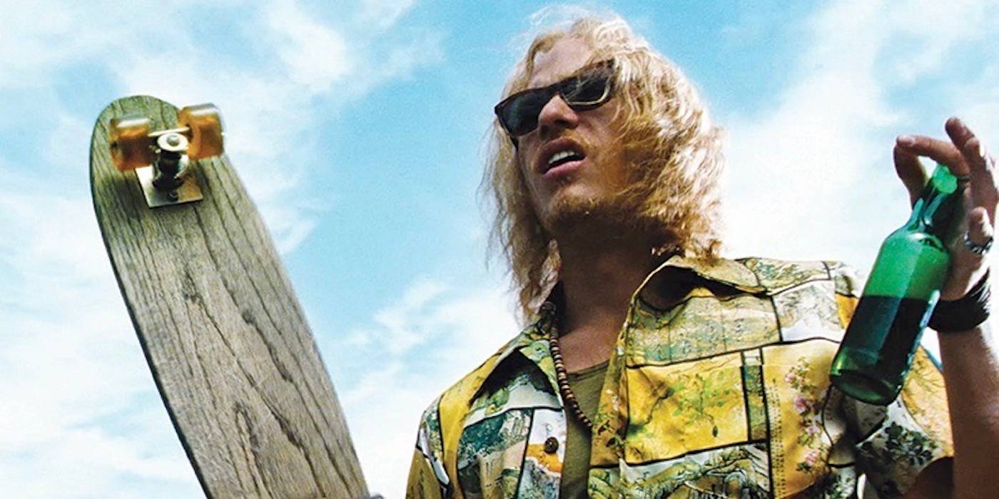 Хет Леджер держит в руках скейтборд и напиток. 