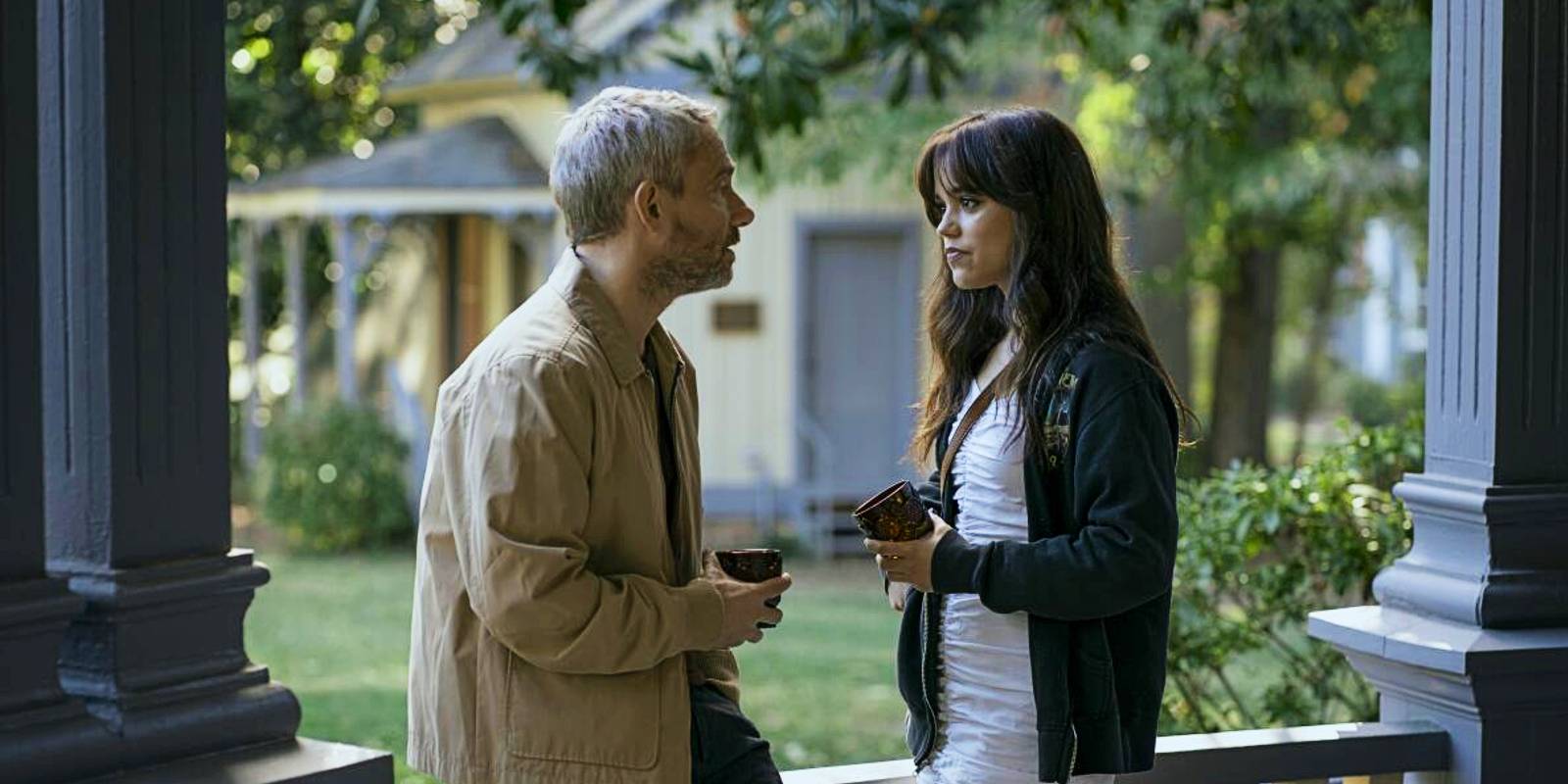 Мистер Миллер и Кайро стоят вместе на веранде, держа в руках напитки в фильме "Миллерс Гёрл"