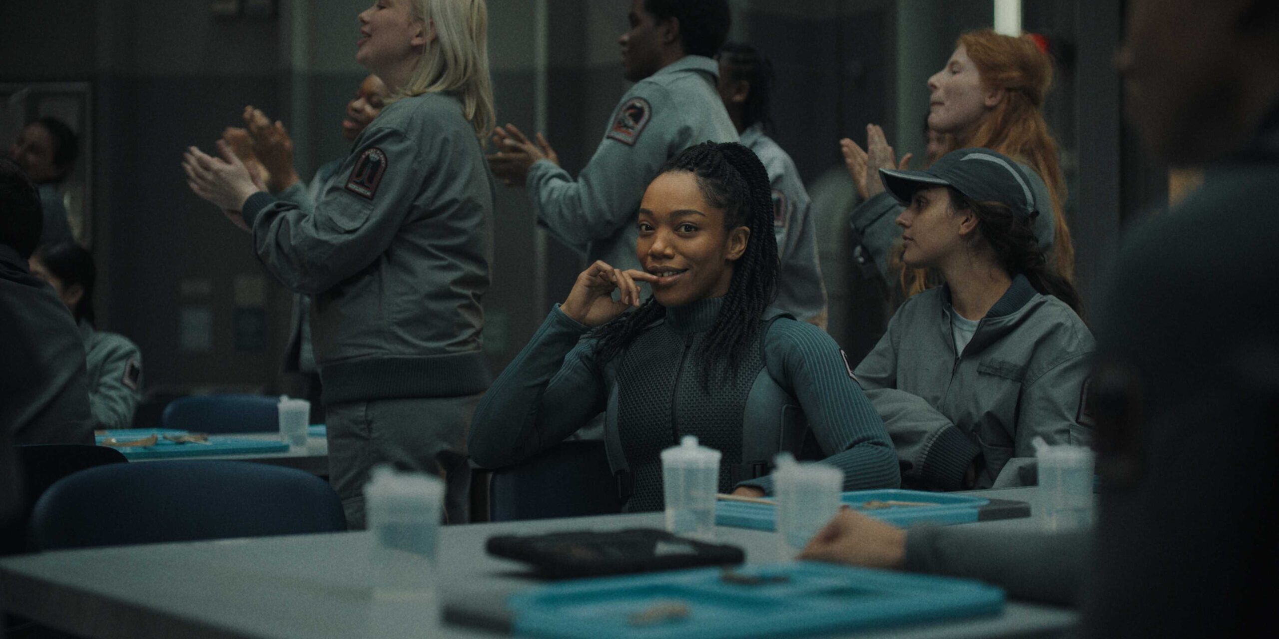 Наша, с лукавой улыбкой смотрящая в камеру из столовой, когда люди аплодируют Мики 17