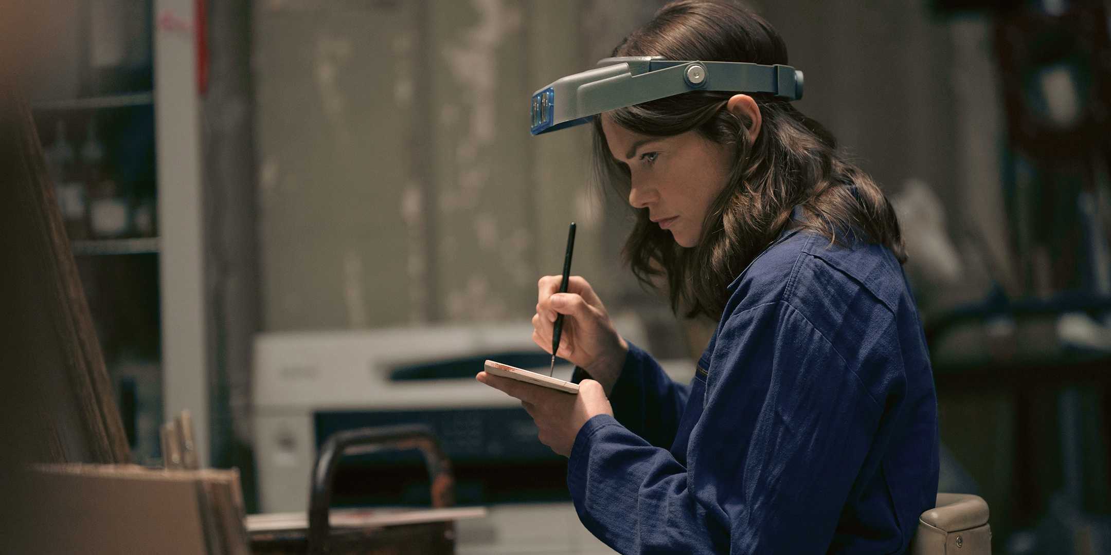 Сара Тьюкер, сыгранная Рут Уилсон, подозрительно смотрит на что-то в мастерской на улице Даун-Кеметри-Роуд