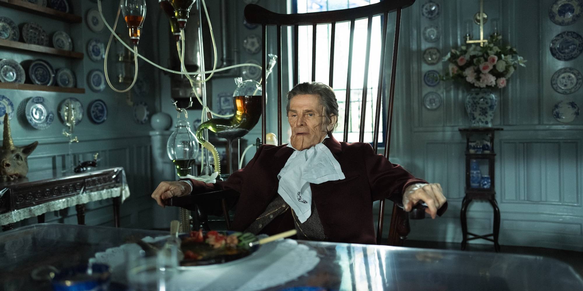 Искалеченный Виллем Дефо, сидящий за столом в фильме "Poor Things".