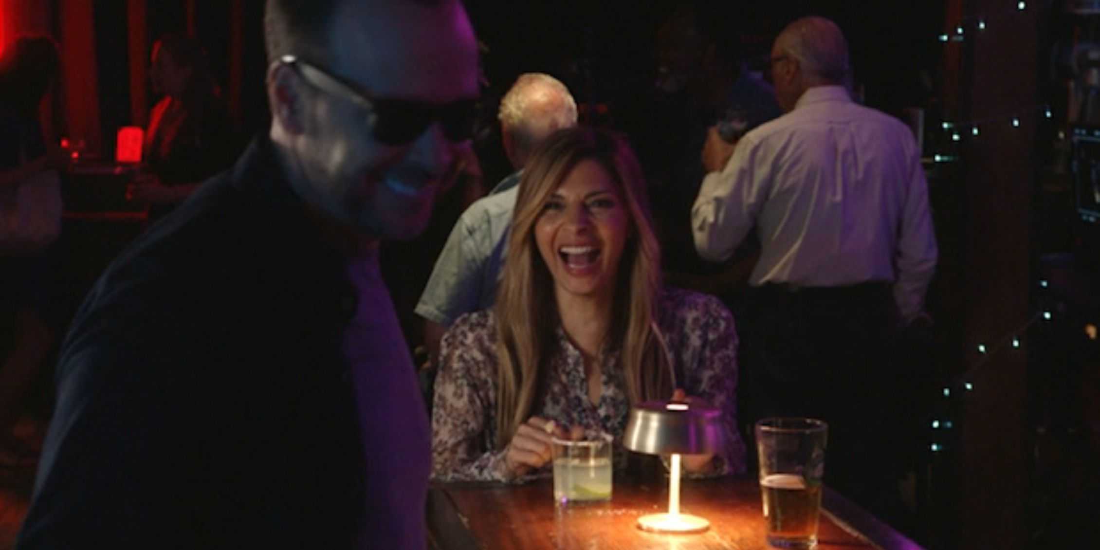 Мэгги из "Blue Bloods" сидит за столом и смеется, а Дэнни стоит рядом в очках и улыбается