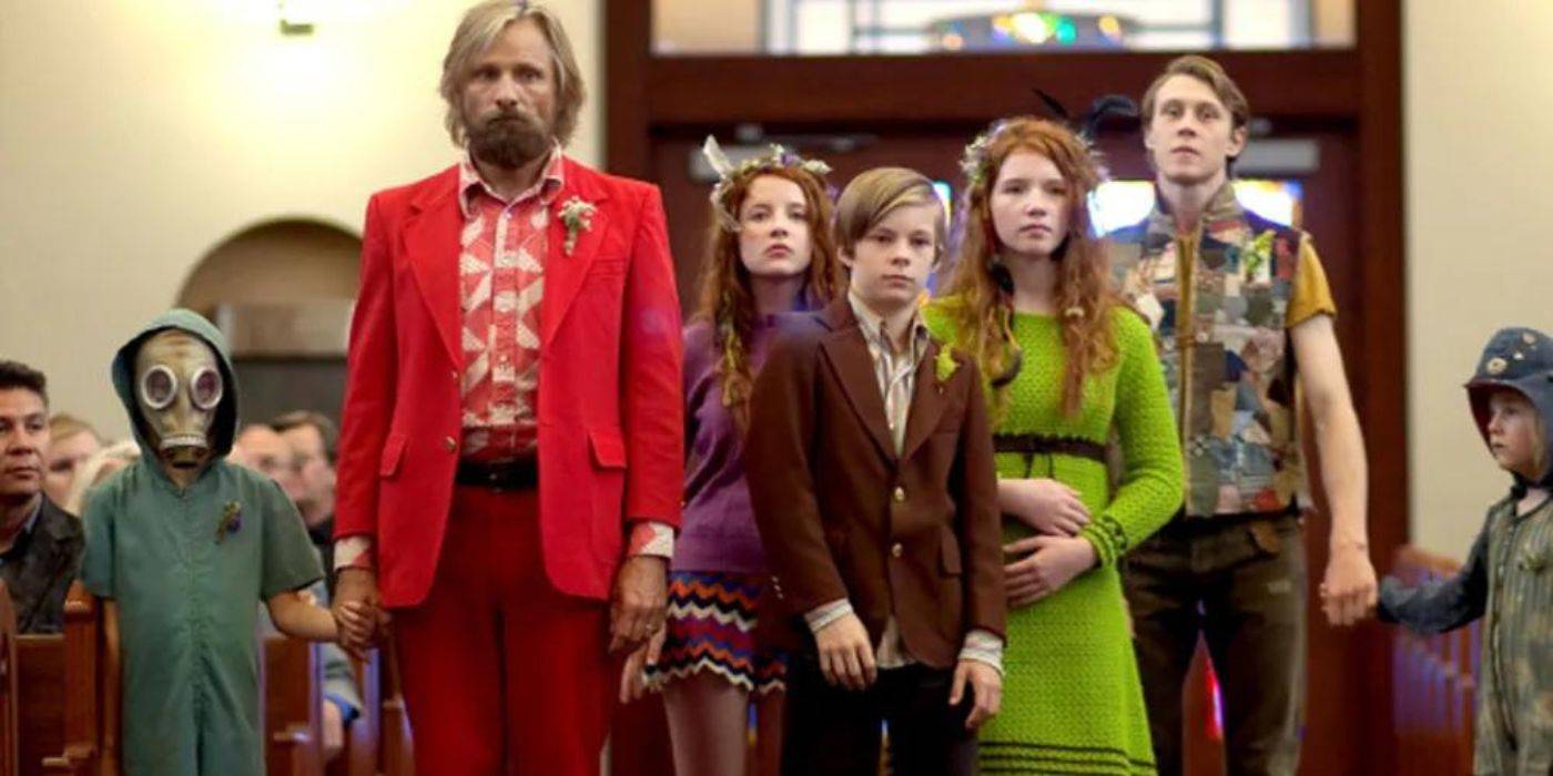 Бен Кеш, одетый в красное, и его большая семья задумчиво стоят посреди церкви, посещая похоронную церемонию матери в фильме "Captain Fantastic"