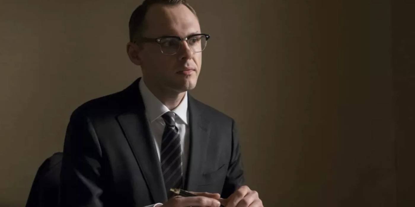 Кристофер Денхэм в роли Клауса Фукса в офисе, держащего ручку в фильме "Оппенгеймер"
