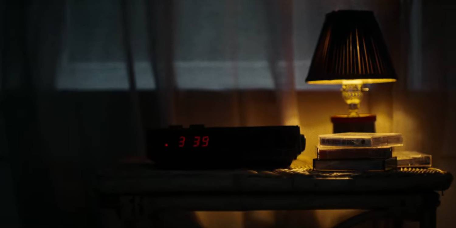 На темном фоне горит лампа рядом с будильником, на котором написано 3:39 в Hell Camp.