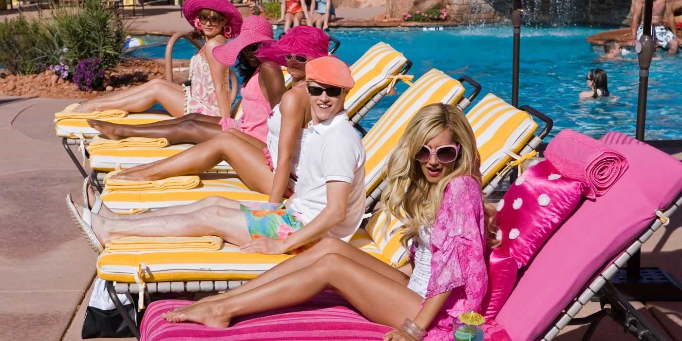 Шарпай (Эшли Тисадел) сидит на розовом диване рядом с Райаном (Лукас Грэбил) и своими друзьями у бассейна в High School Musical 2.