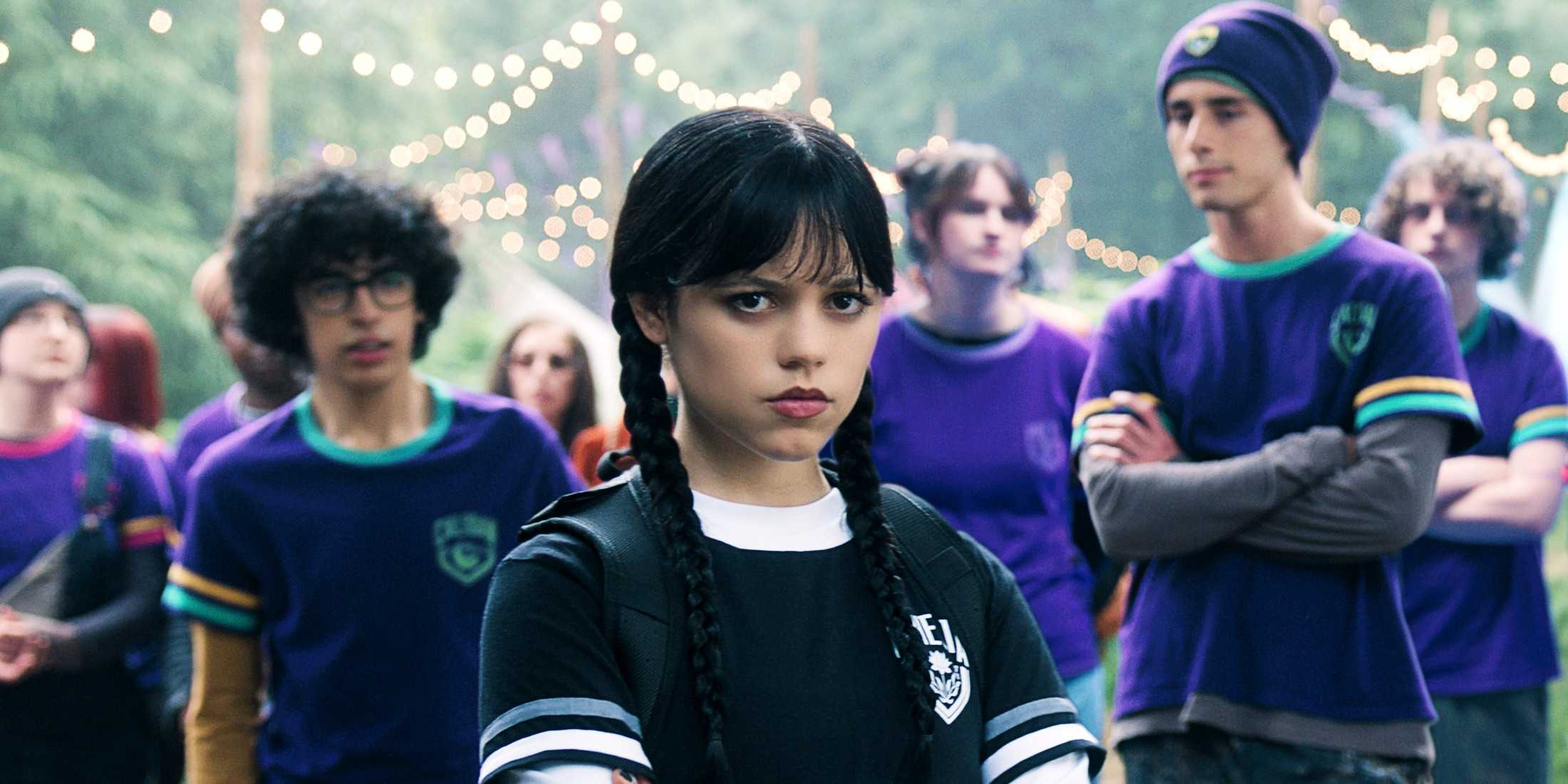 Дженна Ортега в роли Уэнсдей Аддамс, скрещивающая руки с учениками Nevermore за спиной в 2 сезоне "Wednesday"