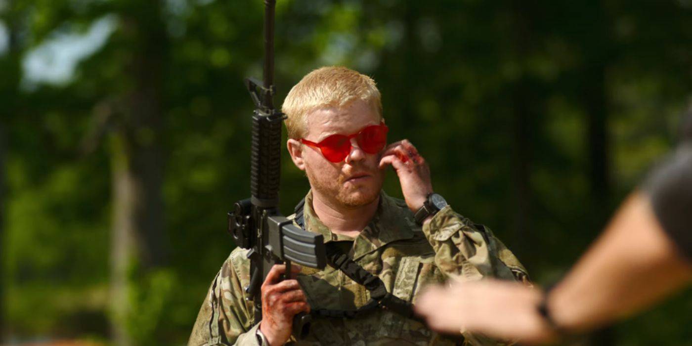 Джесси Племонс в *Гражданской войне* с красными очками, держащий в руках оружие и почесывающий щеку