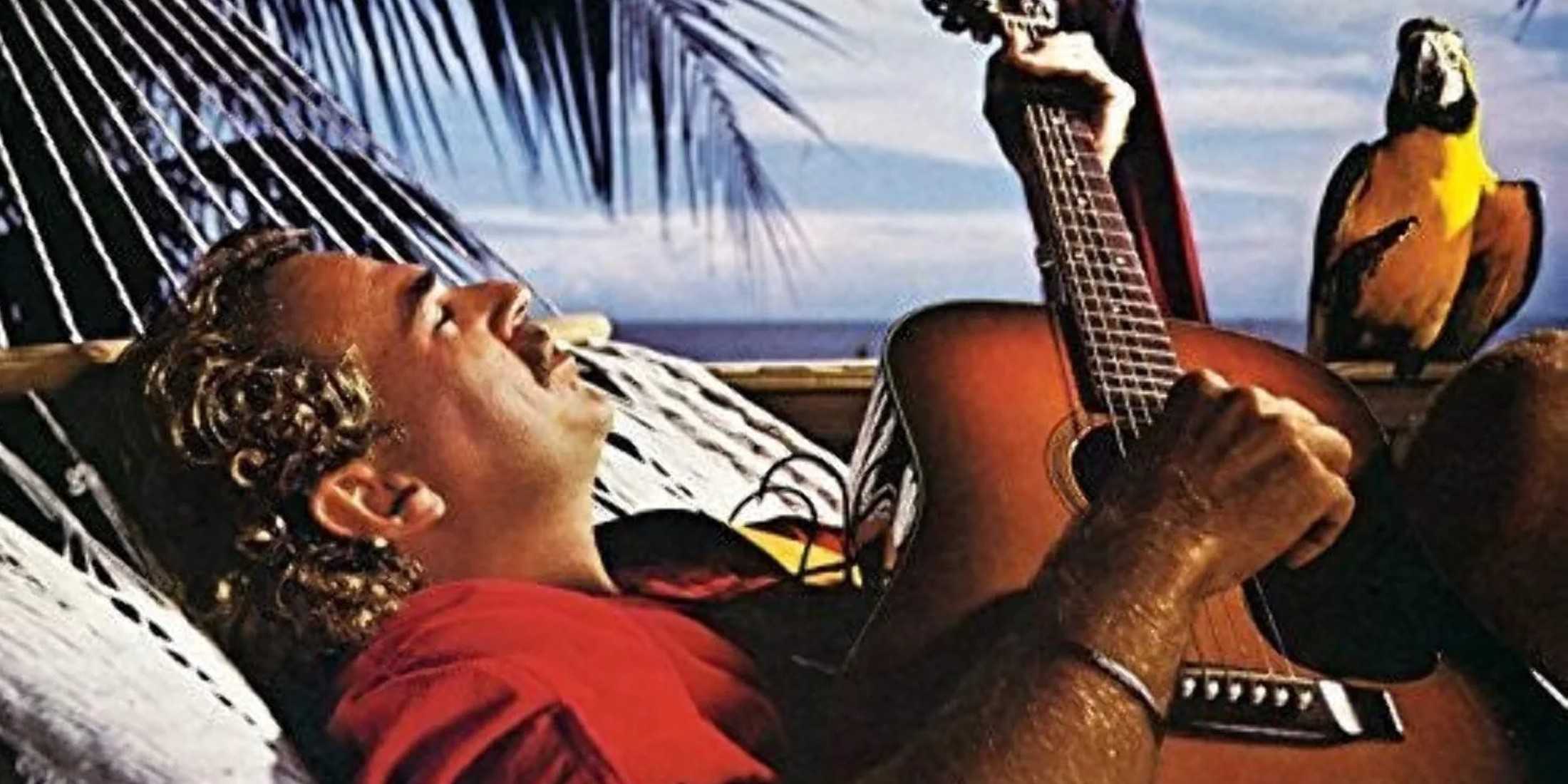 Джимми Баффет лежит в гамаке. Он играет на деревянной гитаре. У него кудрявые волосы средней длины, усы и красная рубашка. Виден желтый попугай. Слева за ним пальма, а вдали можно увидеть голубое небо и океан с облаками.