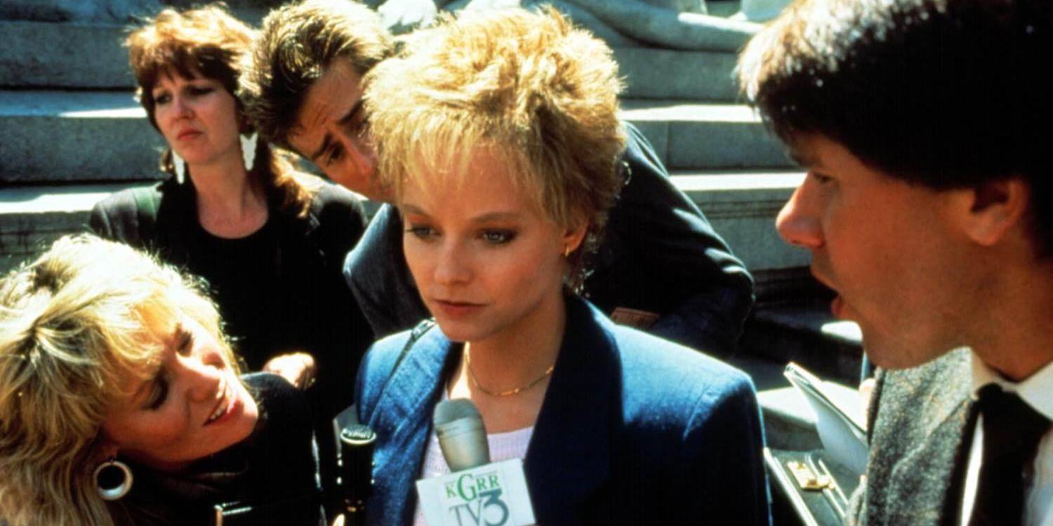 Сара Тобиас (Джидди Фостер) выглядит отстраненной, когда журналисты толкают микрофоны ей в лицо в фильме "Обвиненный" (1988).