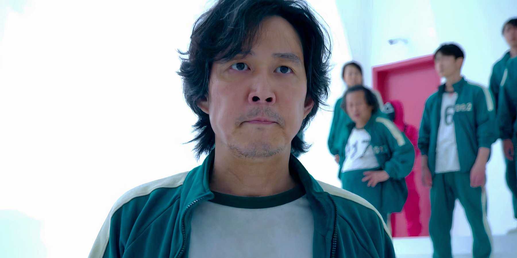 Ли Чун-Дже как Ги-Хун, решительно смотрящий, с другими игроками позади него в первом сезоне "Игра в кальмара"