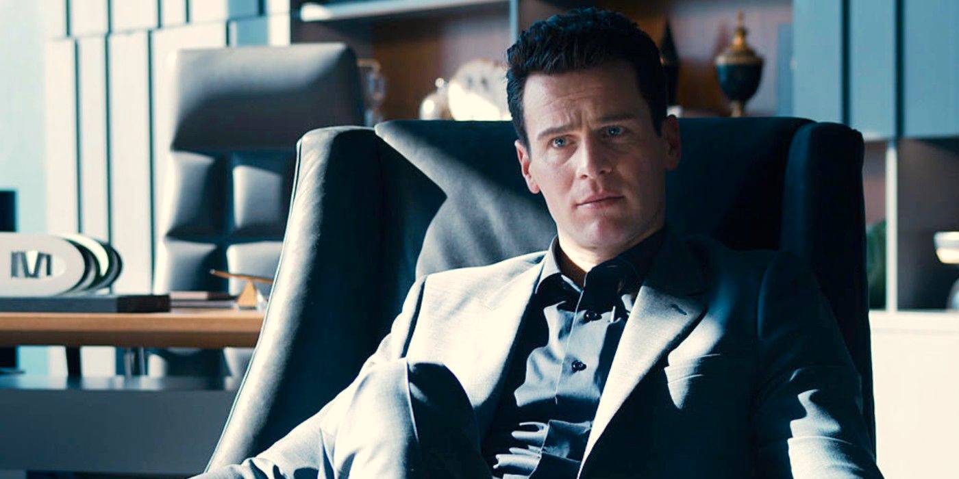 Джонатан Грофф в роли Агента Смита сидит в кресле в современном офисе в фильме "Матрица: Воскрешение"