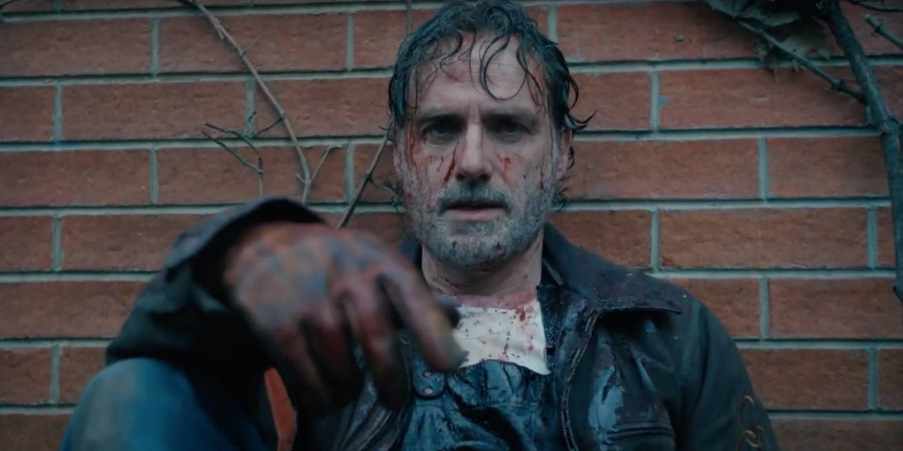 Рик Граймс, истекающий кровью, опирающийся на кирпичную стену в "Ходячих мертвецах: Те, кто живы"