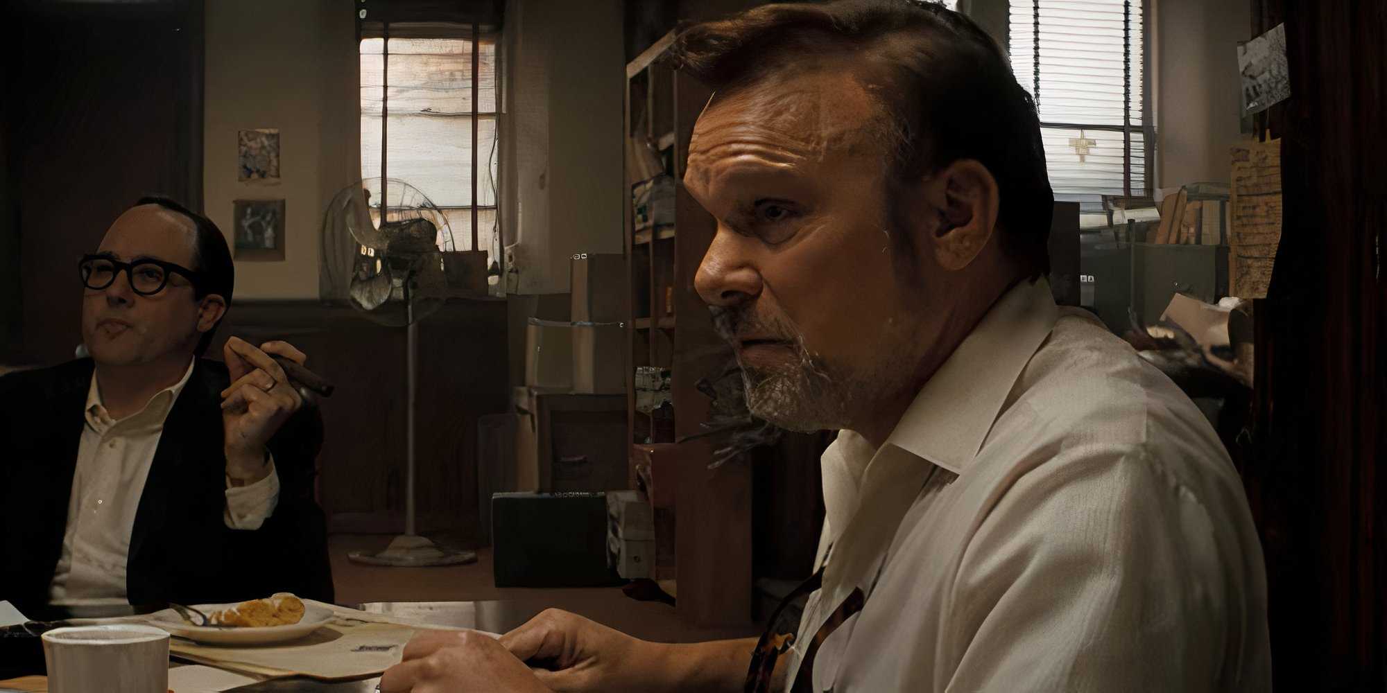 Эйлан Ломакс (Норберт Лео Баут) ест, сидя за столом и обсуждая Боба Дилана.