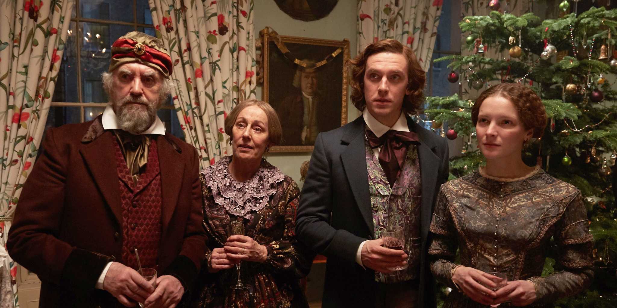 Морфид Кларк и остальные главные актеры, стоящие перед рождественской елкой в фильме "Человек, который изобрел Рождество"