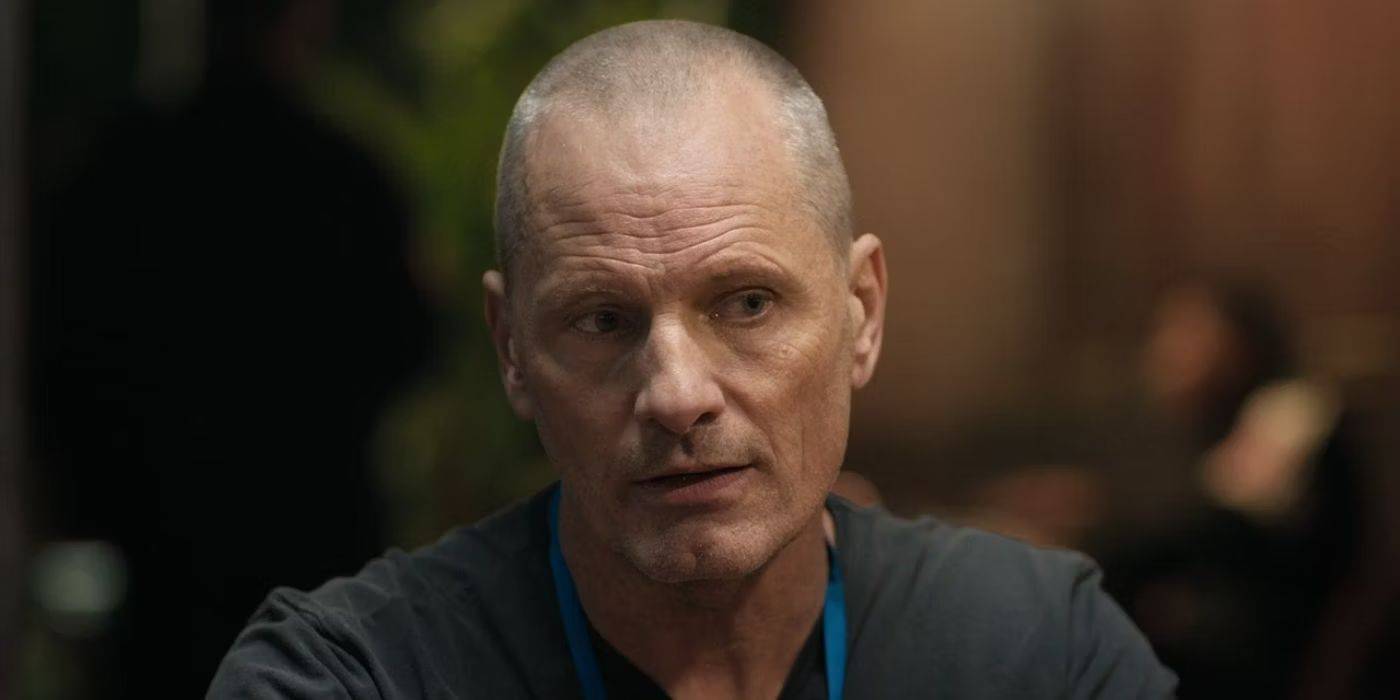 Ричард Стантон сидит, на его лице выражение беспокойства, в то время как коллега отдыхает на заднем плане в фильме "Thirteen Lives"