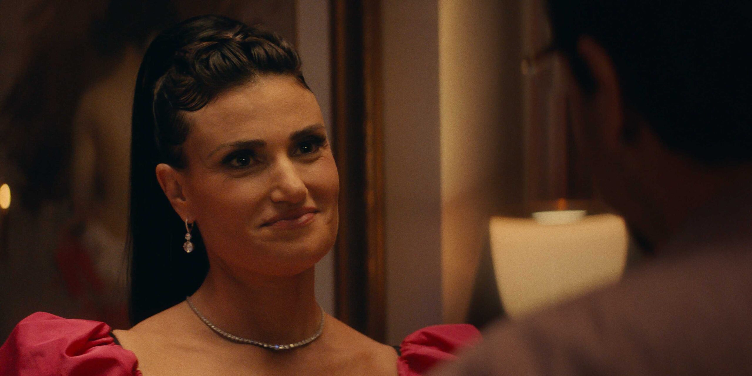 Идина Мэнзел в формальной одежде, улыбающаяся в Uncut Gems